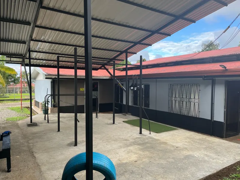 Área de calistenia al aire libre: barras bajo un techo liviano, piso de cemento y una llanta azul.