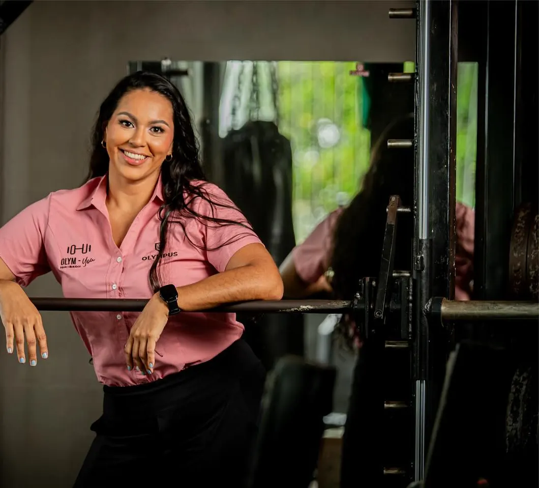 Paola Villalobos, con camisa rosada del gimnasio, sonríe apoyada en una barra dentro de Olympus.