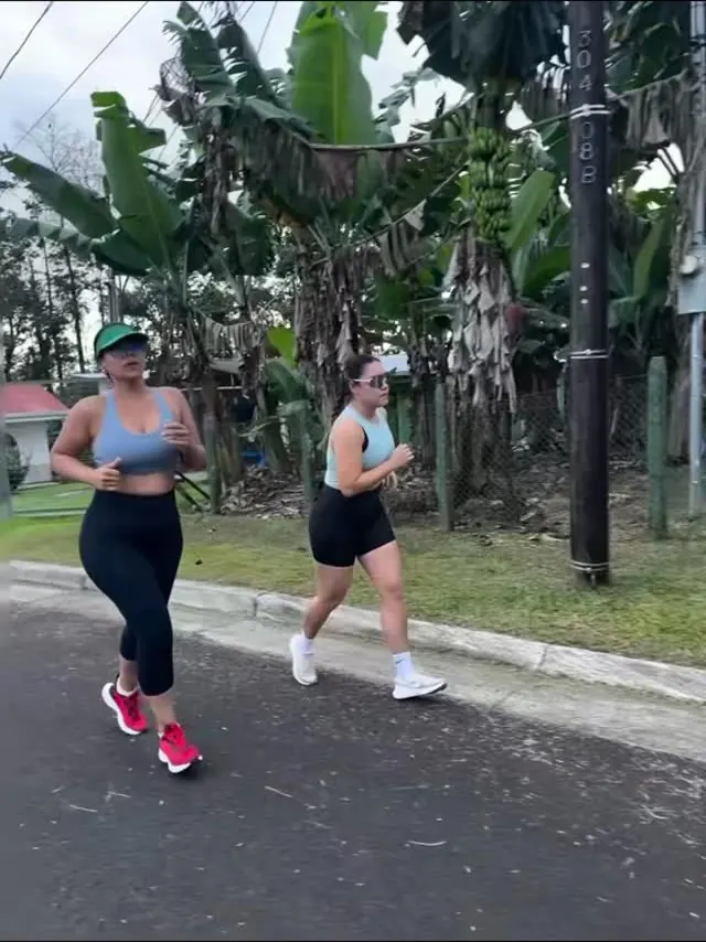 Dos corredoras en ropa deportiva trotan por una calle rural entre matas de banano.